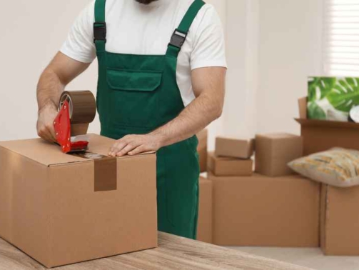 Man packing box with adhesive tape indoors, closeup. Moving service